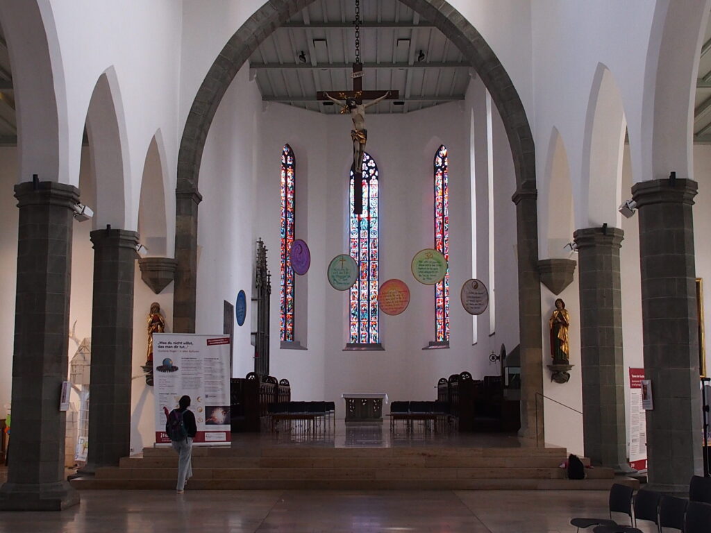 Der Altarraum von Sankt Jodok. Von der Decke hängen runde Scheiben mit der goldenen Regel