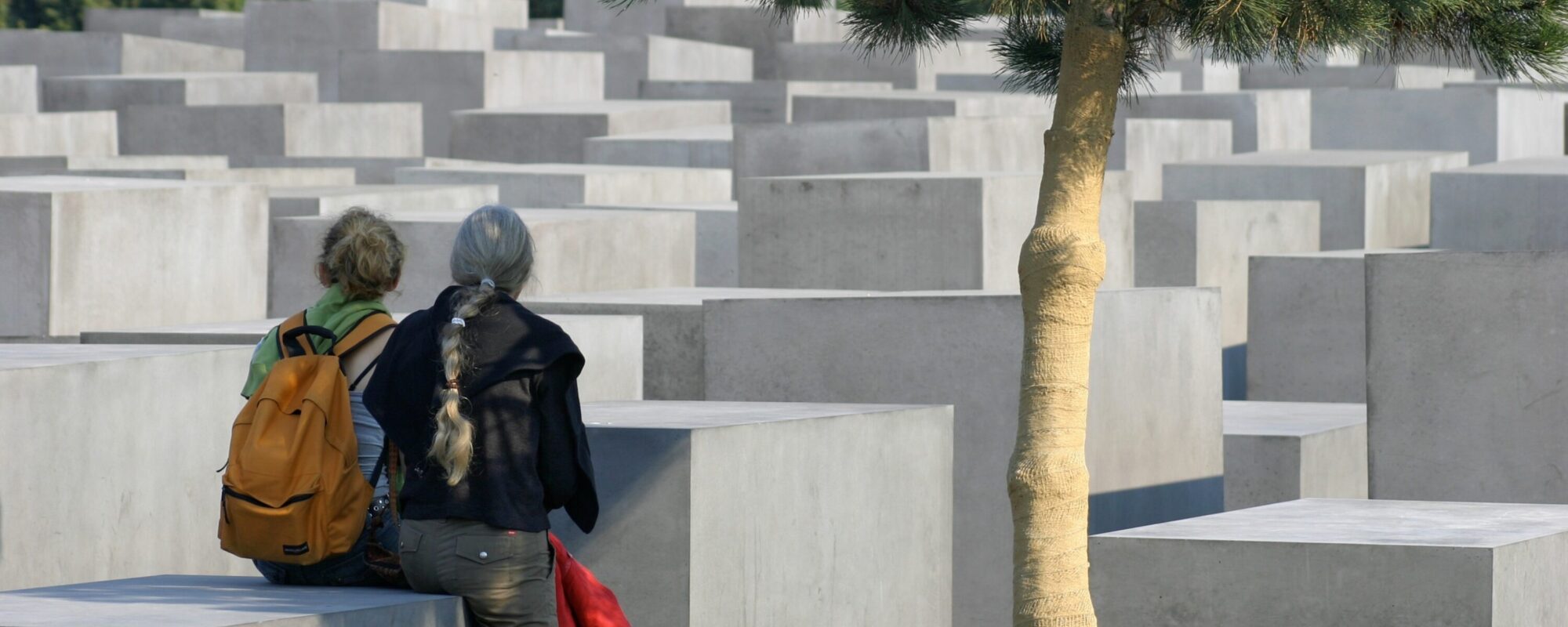 Das Bild zeigt das Holocaust-Mahnmal in Berlin. Zwei Frauen sitzen auf niedrigen Stehlen.