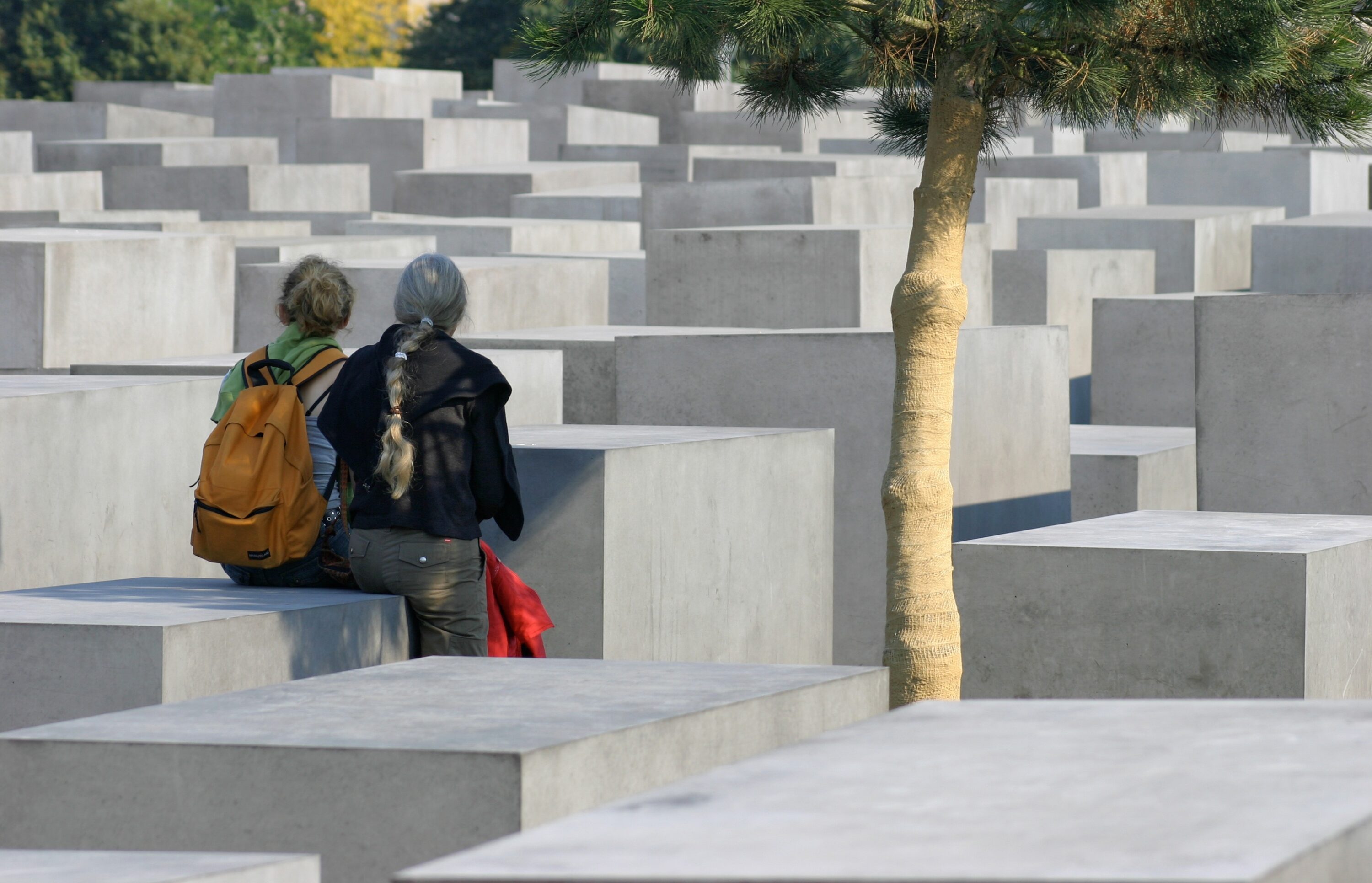 Das Bild zeigt das Holocaust-Mahnmal in Berlin. Zwei Frauen sitzen auf niedrigen Stehlen.
